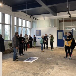 large room with white walls grey floor and a crowd of people looking at art work