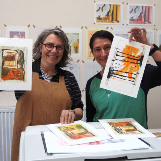 Two smiling women holding their vibrant orange, black and white risograph prints which have been scanned from their sketchbooks.